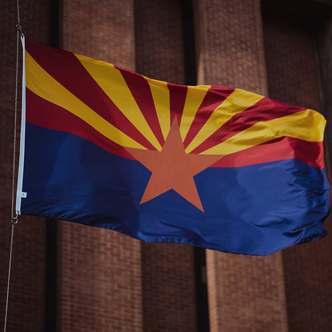 Image of the Arizona State Flag waving in front of a building