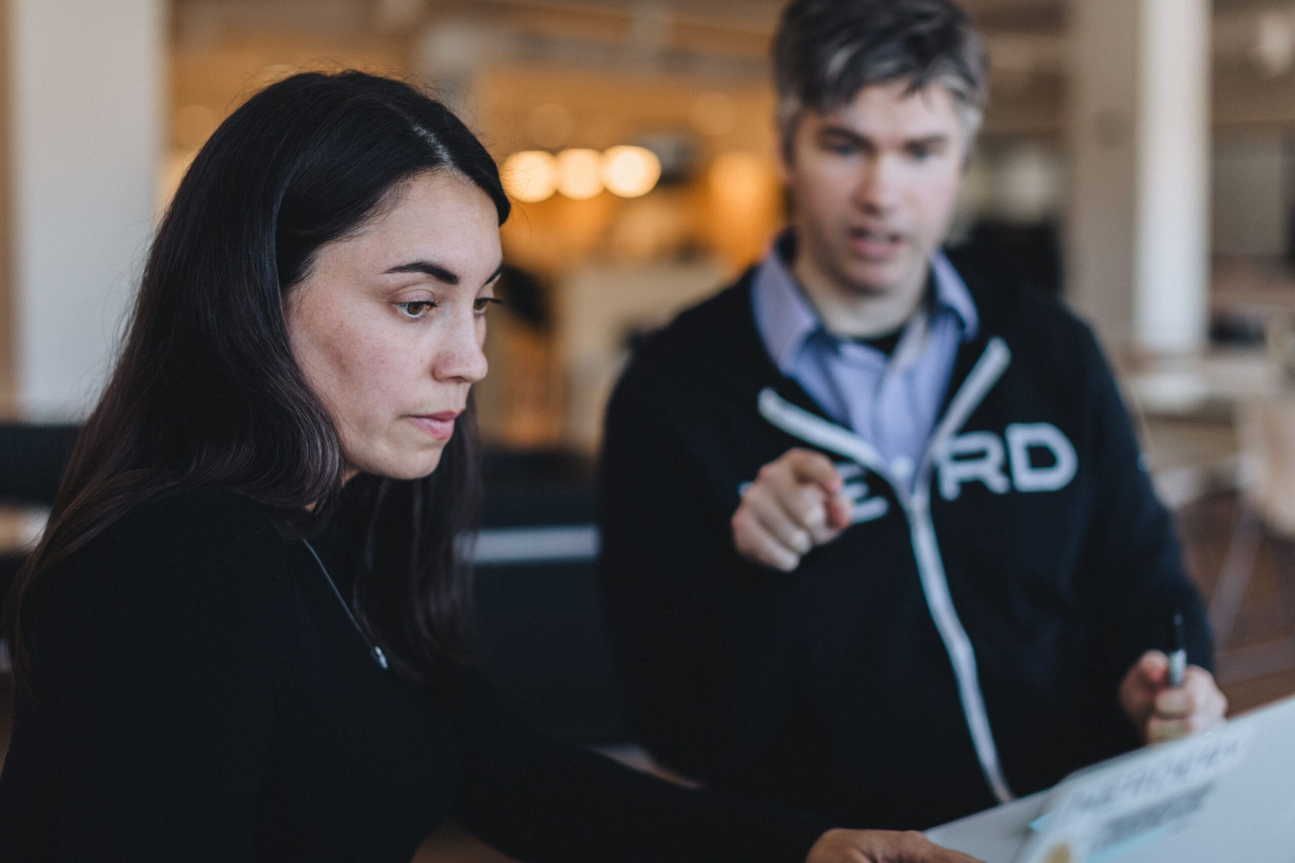 Two Nerdery employees working together at a white table with one pointing at something.