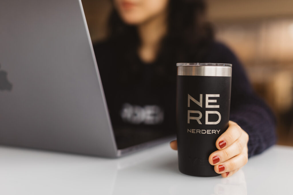 Woman working at a laptop with close up on a Nerdery branded mug
