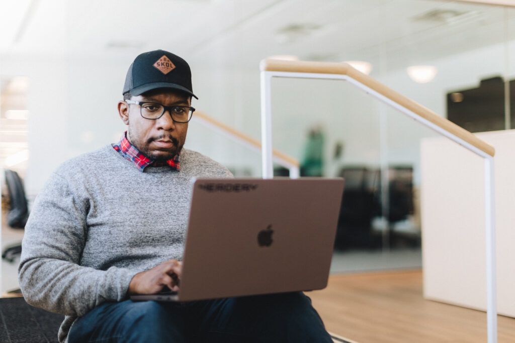 Man with a baseball hat working at a laptop