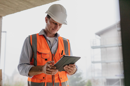 Building contractor evaluating work using digital tablet at incomplete building construction site